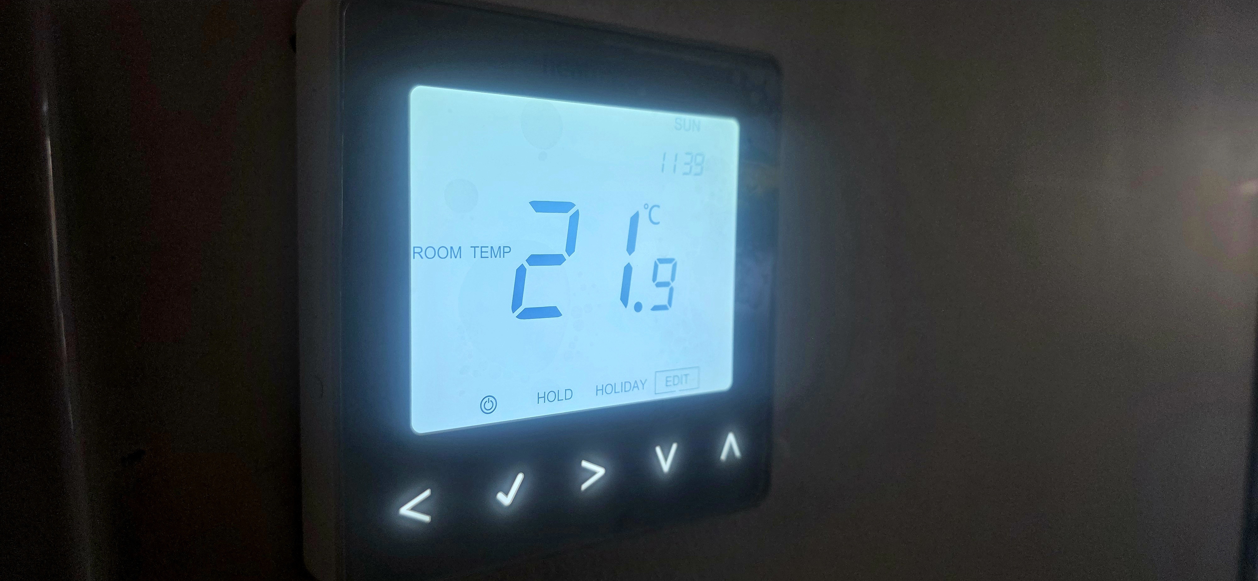 Digital programmable room thermostat on a wall showing a room temperature of 21.9°C